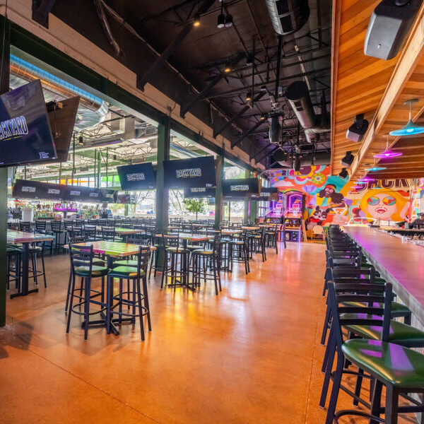 Industrial-style bar with high ceilings, colorful murals, and large flat-screen TVs.