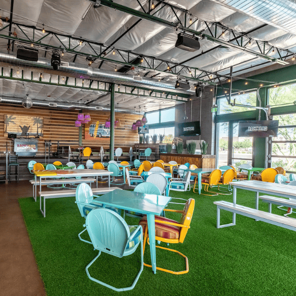 Colorful indoor dining area with retro-style chairs, picnic tables, and artificial turf flooring.