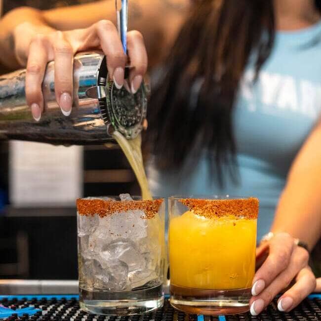 Bartender pouring yellow cocktail into glass with chili powder rim