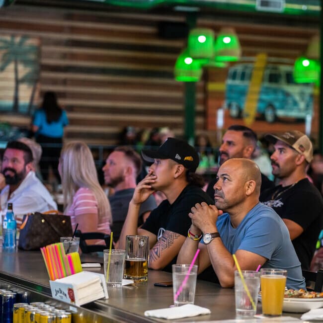 Group of people watching a game at a bar with drinks and food on the counter