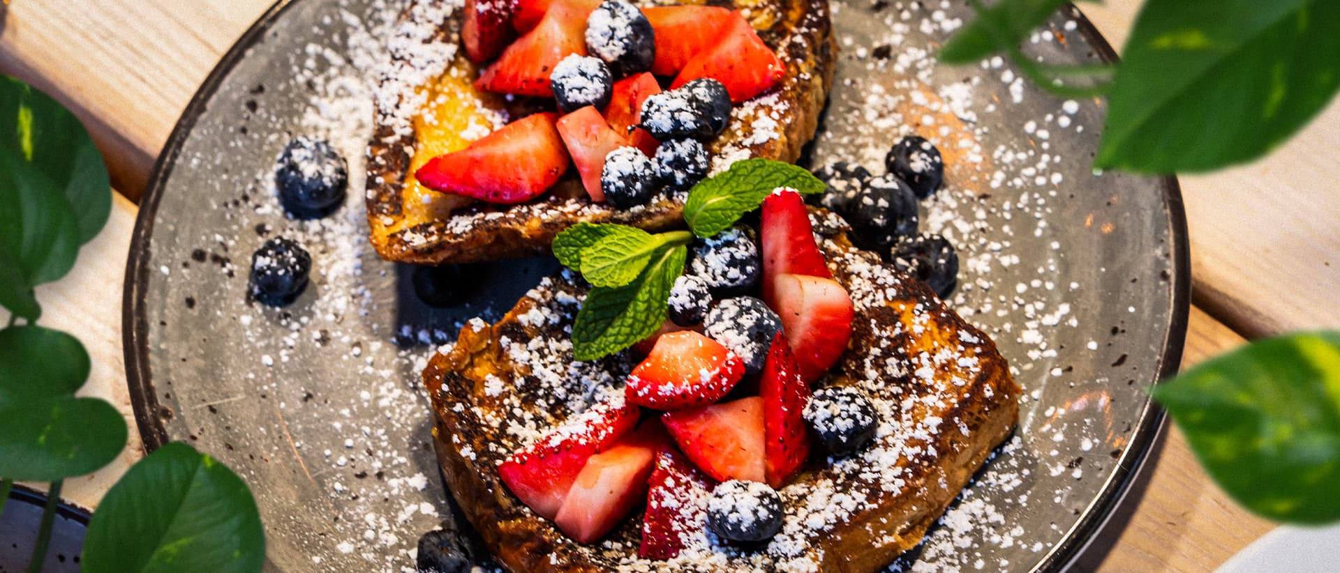 French toast topped with fresh strawberries, blueberries, powdered sugar, and mint garnish served on a rustic plate for weekend brunch.